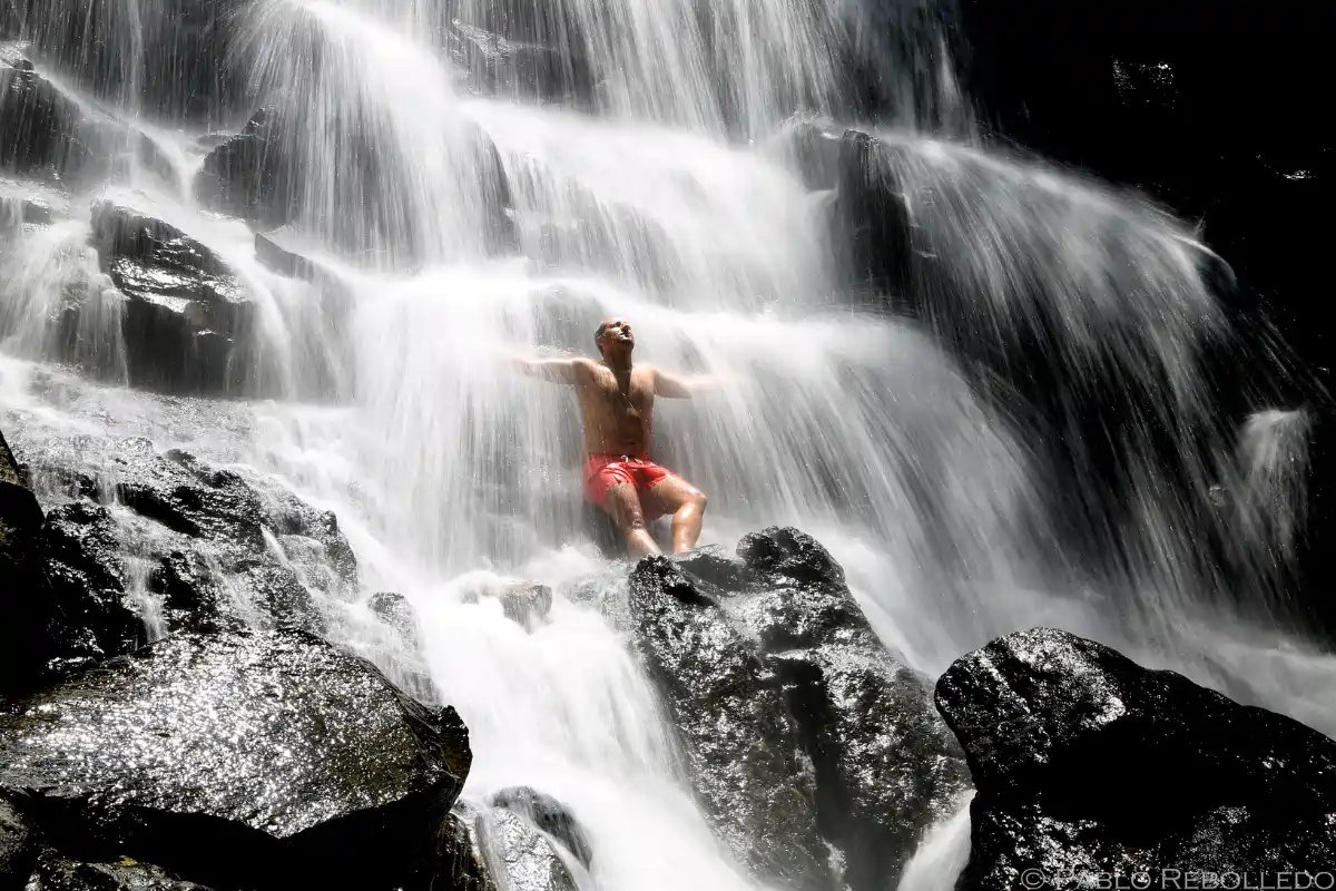 Traveler enjoying a refreshing swim beneath a tropical waterfall in Bali