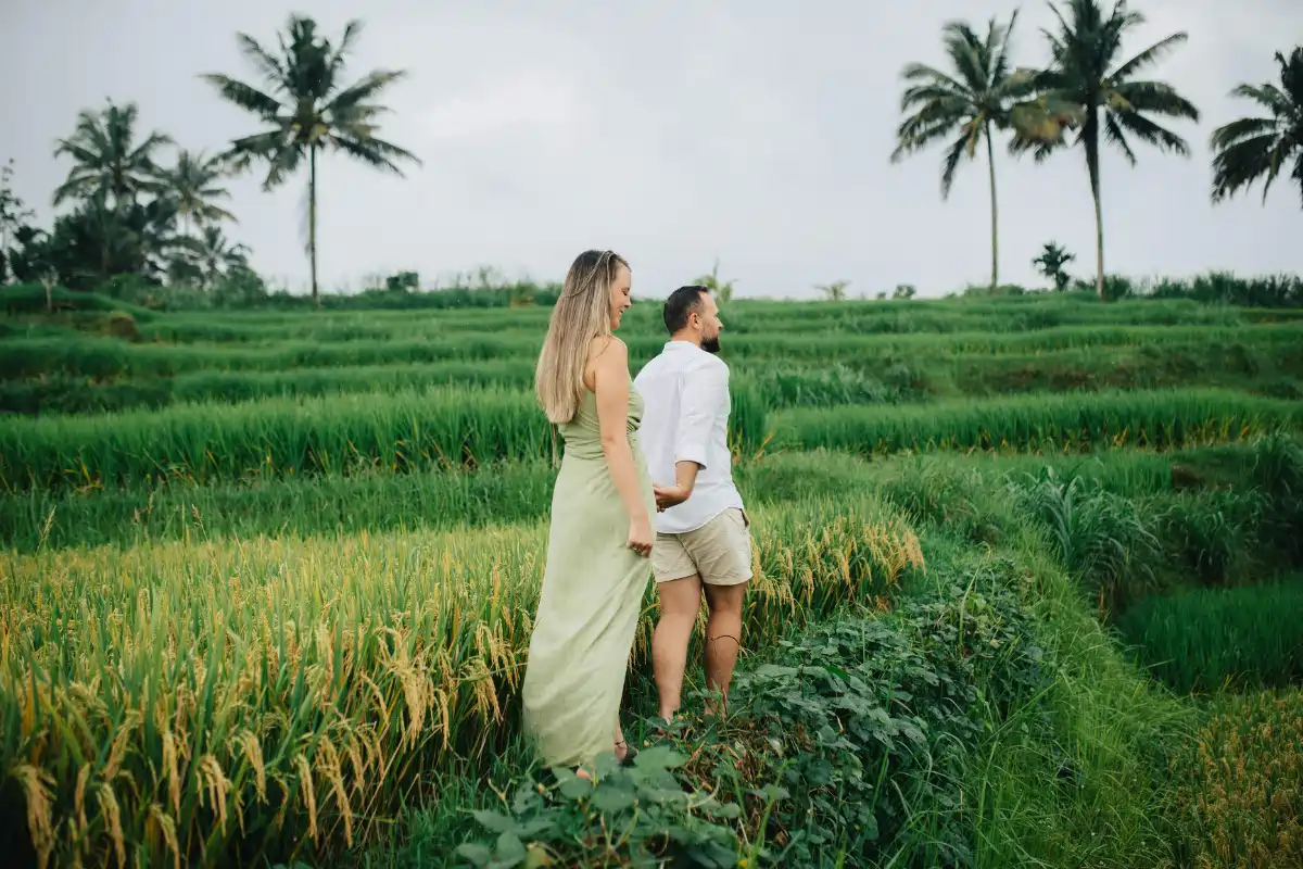 Couple walking through lush green rice fields surrounded by tropical palm trees in Bali